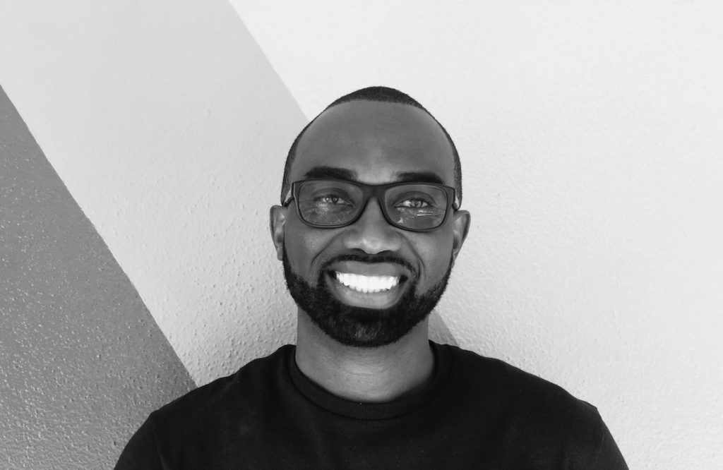 Handy Metellus founder of Dynamik Apps man wearing glasses and a black t-shirt in a classic black and white portrait.